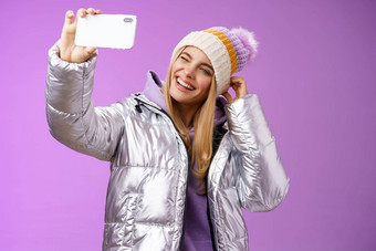 快乐的无忧无虑的迷人的金发碧眼的女孩有趣的想要帖子<strong>图片</strong>滑雪度假胜地假期采取塞夫利持有智能手机模仿显示舌头眨眼移动显示<strong>紫色</strong>的背景