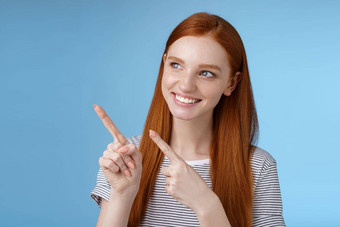 有吸引力的红色头发的人女模型纯清洁皮肤姜长头发指出左感兴趣微笑满意指示有趣的广告感兴趣产品蓝色的背景