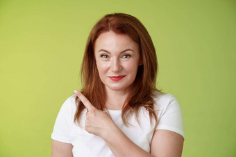 种类快乐的好看的中年女人红色头发的人白色t恤微笑适度的保证给建议指出上左角落里指示伟大的促销活动广告产品绿色背景