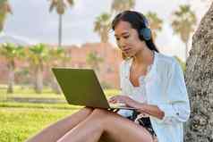 年轻的女人耳机工作移动PC在户外