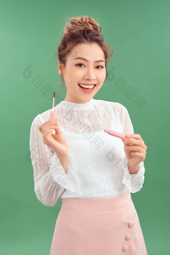 快乐的年轻的亚洲女人应用口红孤立的绿色背景