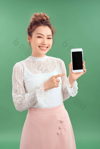 惊讶快乐亚洲女人显示空白智能手机屏幕指出孤立的绿色背景