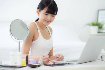 美年轻的亚洲女人学习化妆刷脸颊移动PC电脑教程在线女教学解释使化妆品流媒体社会媒体