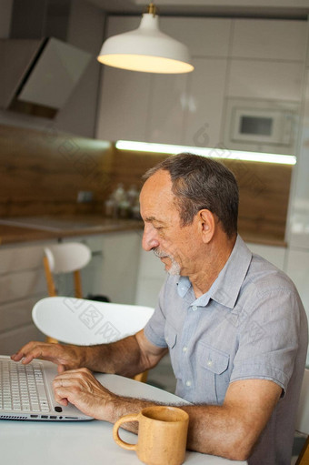 时尚的成熟的男人。工作首页移动PC坐着表格厨房快乐退休家庭办公概念