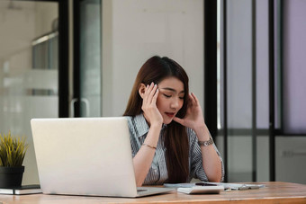 强调年轻的女人坐着桌子上工作首页办公室女商人头疼问题工作办公室