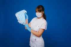 年轻的女孩医生医疗面具持有很多面具手护士提出了蓝色的背景