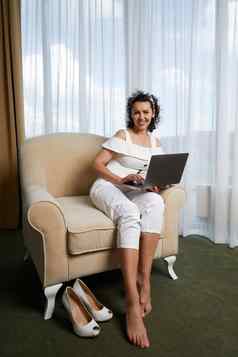 美丽的年轻的女人移动PC坐着扶手椅概念放松业务夫人酒店房间
