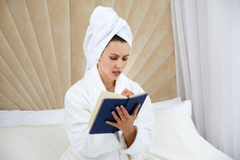 年轻的女人坐在床上穿浴袍写作笔记日记博主创造了出版博客笔记本