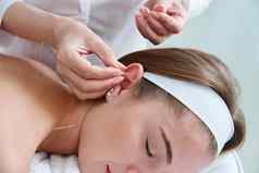 美丽的女人放松床上针灸治疗针耳朵替代治疗概念