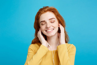 生活方式概念肖像快乐的快乐姜红色的头发女孩享受听音乐耳机快乐的微笑相机孤立的蓝色的柔和的背景复制空间