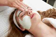 美容师应用振兴面部面具女脸美沙龙面部治疗概念