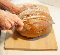 上了年纪的女人的手减少轮黑麦面包面粉厨房董事会