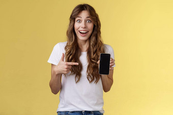 惊讶快乐幸运的女孩赢得在线互联网彩票微笑广泛的持有智能<strong>手机</strong>指出空白移动电话屏幕显示显示咧着嘴笑兴奋热情的站黄色的背景