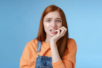 强烈的担心害怕不确定年轻的红色头发的人恐慌愚蠢的女孩皱着眉头心烦意乱焦虑咬指甲<strong>情感</strong>害怕解雇了站蓝色的<strong>背景情感</strong>吓坏了