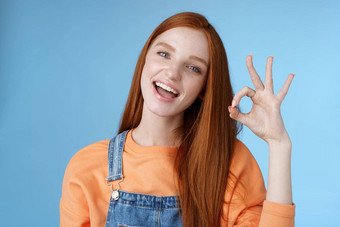 工作室拍摄无忧无虑的快乐有吸引力的欧洲红色头发的人女孩显示标志微笑白色牙齿批准确认推荐好产品同意条款给积极的反馈的想法完美的
