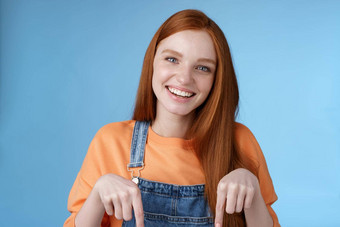 友好的快乐红色头发的人女孩微笑活泼的漂亮的露齿而笑指出指数手指提供好提供推荐服务站蓝色的背景讨论有趣的产品蓝色的背景