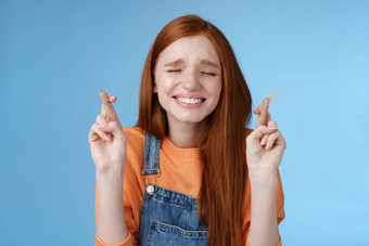 真诚的充满希望的可爱的红色头发的人女孩奇迹关闭眼睛忠实地祈祷交叉手指好运气希望梦想真正的使<strong>急切</strong>的听到积极的结果期待蓝色的背景