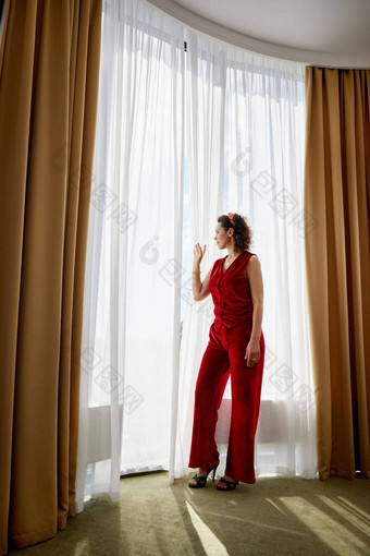 美丽的年轻的卷曲的女人站窗帘大全景窗口
