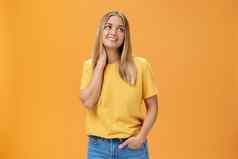 漂亮的温柔的可爱的欧洲女独立的自由职业者黄色的t恤叹息触碰脖子盯着梦幻上角落里愉快的微笑摆姿势橙色背景
