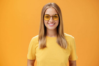 时尚的自信的迷人的欧洲女人公平头发晒黑皮肤黄色的t恤太阳镜微笑广泛的逗乐快乐的盯着相机摆姿势橙色背景