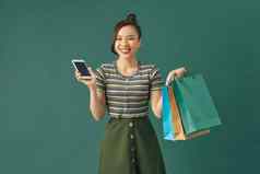 在线购物美丽的年轻的女人持有购物袋智能手机微笑站绿色背景