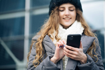 快乐的年轻的女好情绪打字滚动智能手机在户外冬天概念女智能手机站快乐女孩员工打字手机