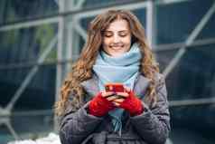 快乐的卷发年轻的女发短信智能手机站街冬天城市一年女攻丝手机在户外在线购物
