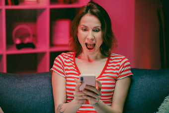 女人持有聪明的电话<strong>手机屏幕</strong>笑享受移动应用程序购物有趣的玩游戏聊天社会媒体坐沙发上首页