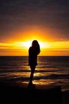 华丽的轮廓女人长头发站海滩发光太阳照明大纲橙色黄色的颜色反映水封面天空
