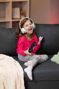 女孩坐着沙发玩视频生活房间首页兴奋玩家女孩手持有操纵杆玩控制台游戏无线控制器有趣的享受快乐表达式