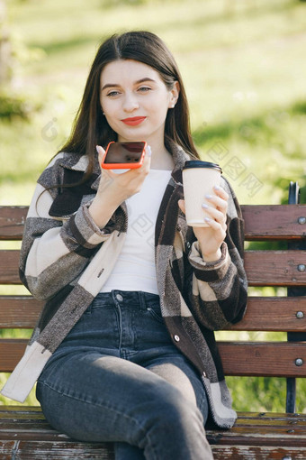 女孩聪明的电话的声音识别音频消息演讲函数女人时尚的休闲装坐在板凳上城市公园