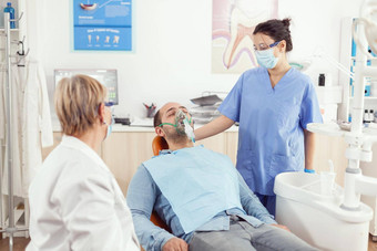医院助理把氧面具生病的男人。病人口腔学手术
