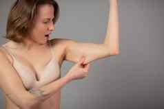 胖乎乎的女人捏上手臂脂肪孤立的灰色背景关闭高加索人女手检查松弛皮肤身体控制时间饮食重量损失概念
