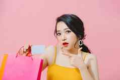 快乐购物狂肖像快乐的亚洲女孩色彩斑斓的购物袋信贷卡孤立的粉红色的背景