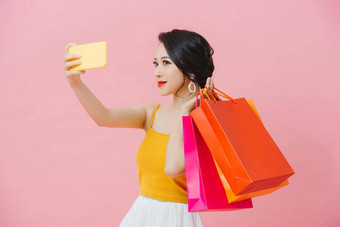 有吸引力的年轻的女人穿夏天装站孤立的粉红色的背景采取自拍携带购物袋