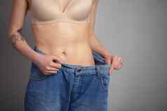年轻的女人显示重量损失穿牛仔裤苗条的女孩大牛仔裤显示失去重量开始吃健康的食物