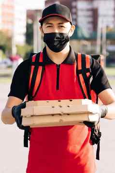 肖像快递交付男人。红色的背包持有披萨纸箱盒子穿保护脸面具手套交付服务优秀的交付