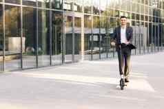 年轻的商人骑电踏板车业务会议办公室办公室建筑业务男人。电运输生态运输e-skateboard环保运输