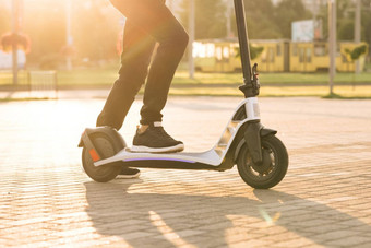 腿赶时髦的人黑色的运动鞋骑电踏板车路工作现代快速度开车电运输e-scooter骑手男人。骑分享租金个人生态运输