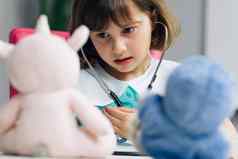 可爱的可爱的学前教育孩子女孩穿医疗统一的持有听诊器听生病的玩具病人聪明的小孩子玩医院游戏医生假装护士概念
