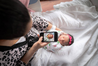 妈妈。粉红色的动物打印浴袍坐在医院床上持有新生儿婴儿女孩披着毯子采取照片移动细胞电话分享家庭朋友