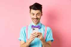 在线购物快乐的家伙智能手机屏幕阅读消息微笑站粉红色的背景