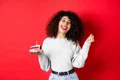 庆祝活动假期概念快乐美丽的女人跳舞使生日持有生日蛋糕微笑站红色的背景