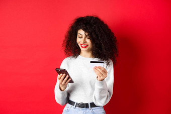 电子商务在线购物概念有吸引力的高加索人女人支付购买互联网持有智能手机信贷卡红色的背景