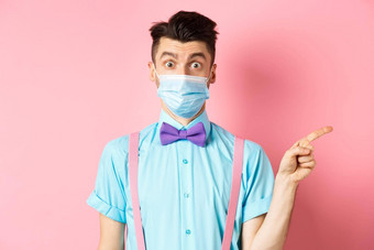 冠状病毒医疗保健检疫概念男人。惊讶医疗面具问题指出好奇的促销提供站粉红色的背景