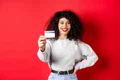 图像现代女人卷曲的头发扩展手显示塑料信贷卡推荐银行购物提供红色的背景