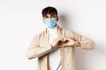 健康科维德检疫概念浪漫的年轻的男人。无菌医疗面具显示心手势胸部爱站白色背景