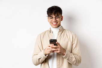 真正的人自然年轻的男人。阅读消息移动电话微笑智能手机屏幕站白色背景
