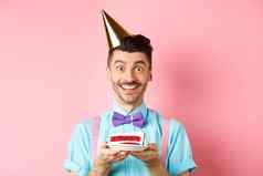 假期庆祝活动概念快乐的年轻的男人。庆祝生日聚会，派对他持有生日蛋糕蜡烛使微笑快乐相机粉红色的背景