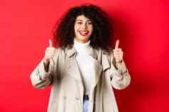 肖像年轻的女人快乐穿沟外套显示竖起大拇指批准赞美好红色的背景